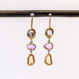 A pair of drop earrings featuring different colored freeform cut sapphires set in different ways in yellow gold.