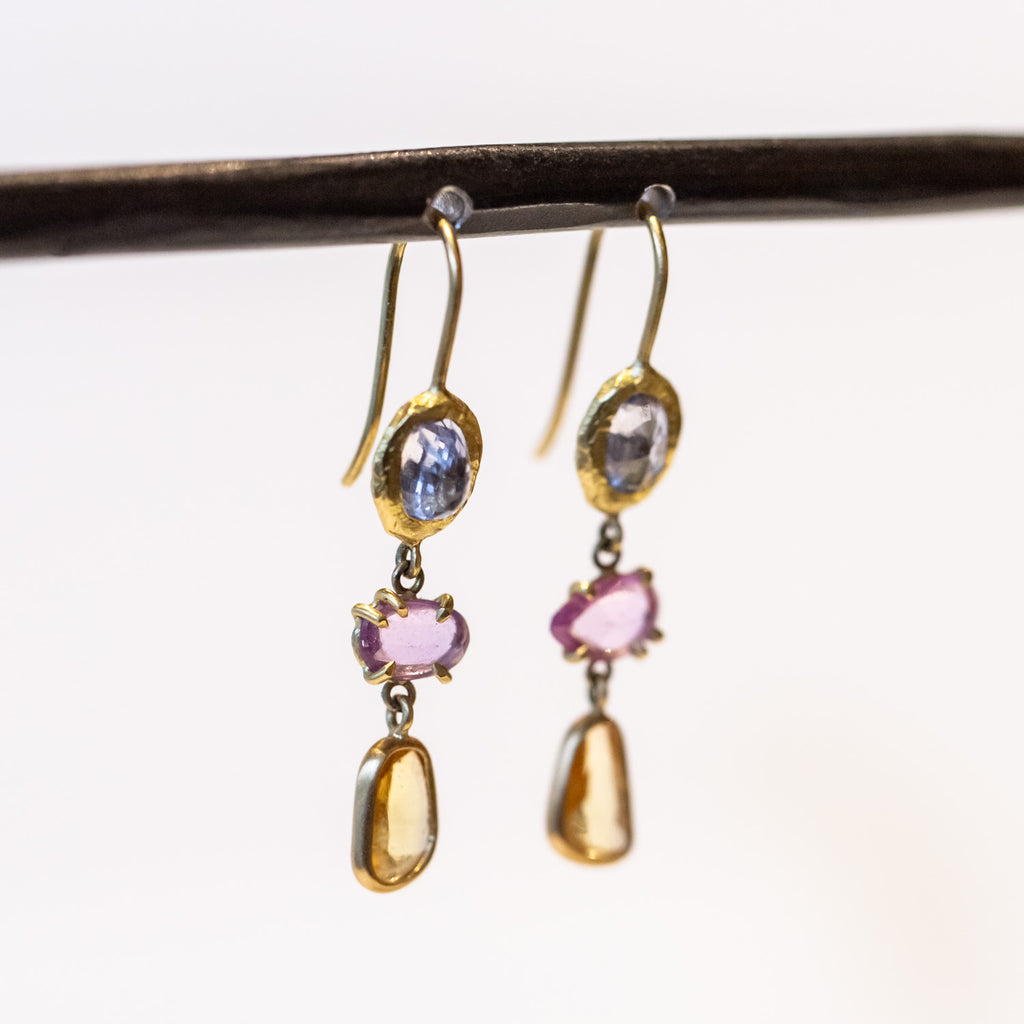 A pair of drop earrings featuring different colored freeform cut sapphires set in different ways in yellow gold.