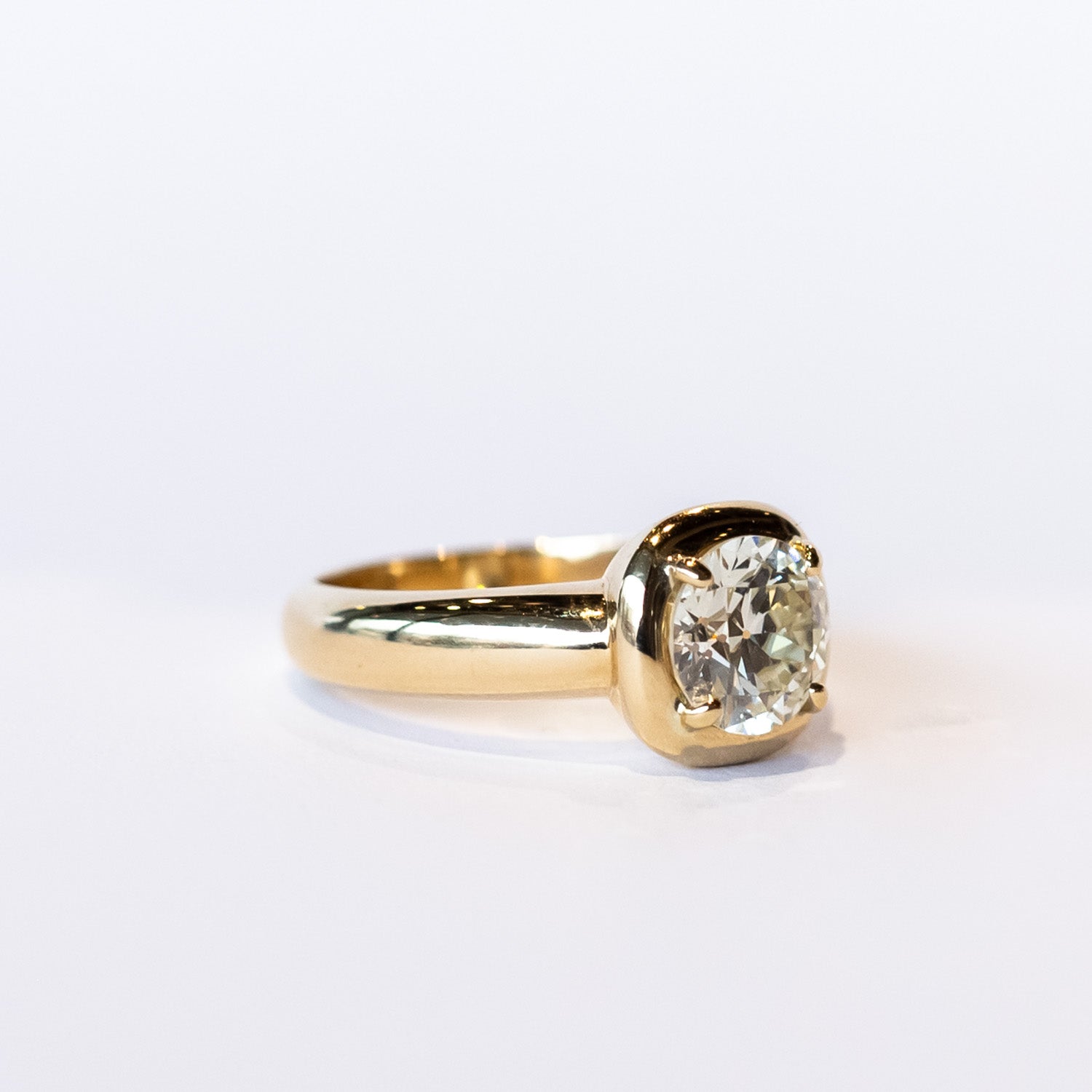 A chunky gold solitaire engagement ring featuring an old mine European cut diamond prong set into a cushion-like setting.