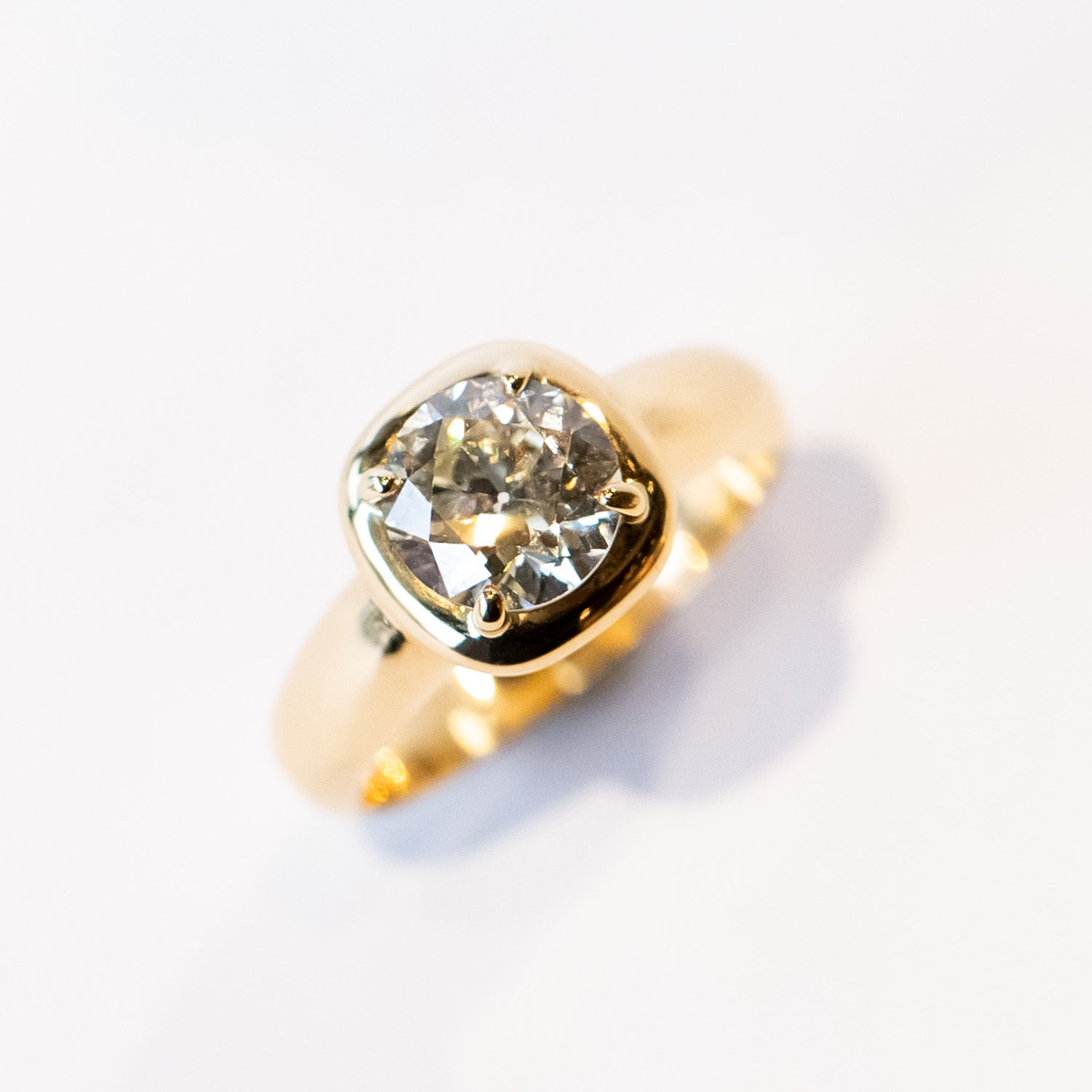 A chunky gold solitaire engagement ring featuring an old mine European cut diamond prong set into a cushion-like setting.