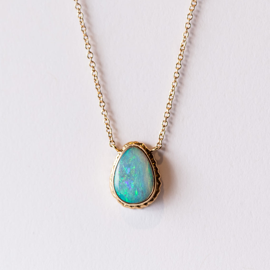 A teardrop shaped opal is bezel set in yellow gold, stationed at the center of a cable chain necklace.