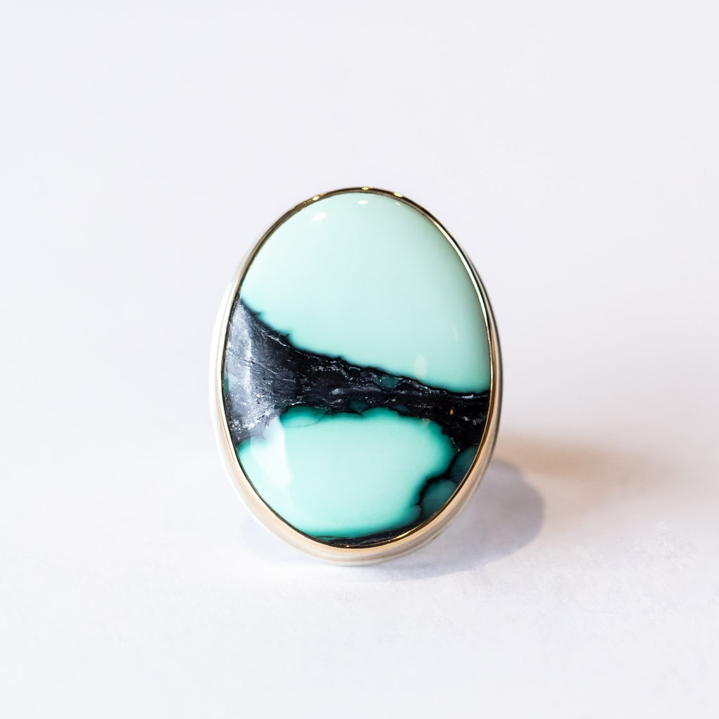 A large oval cabochon Emerald Rose variscite is bezel set in yellow gold on a silver ring.