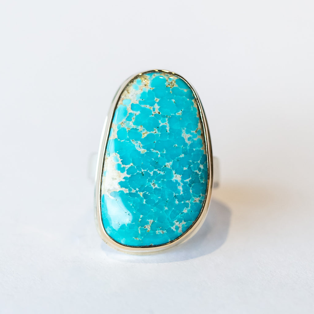 A large, vertical orientated asymmetrical Kingman turquoise gemstone is bezel set in yellow gold on a silver ring.