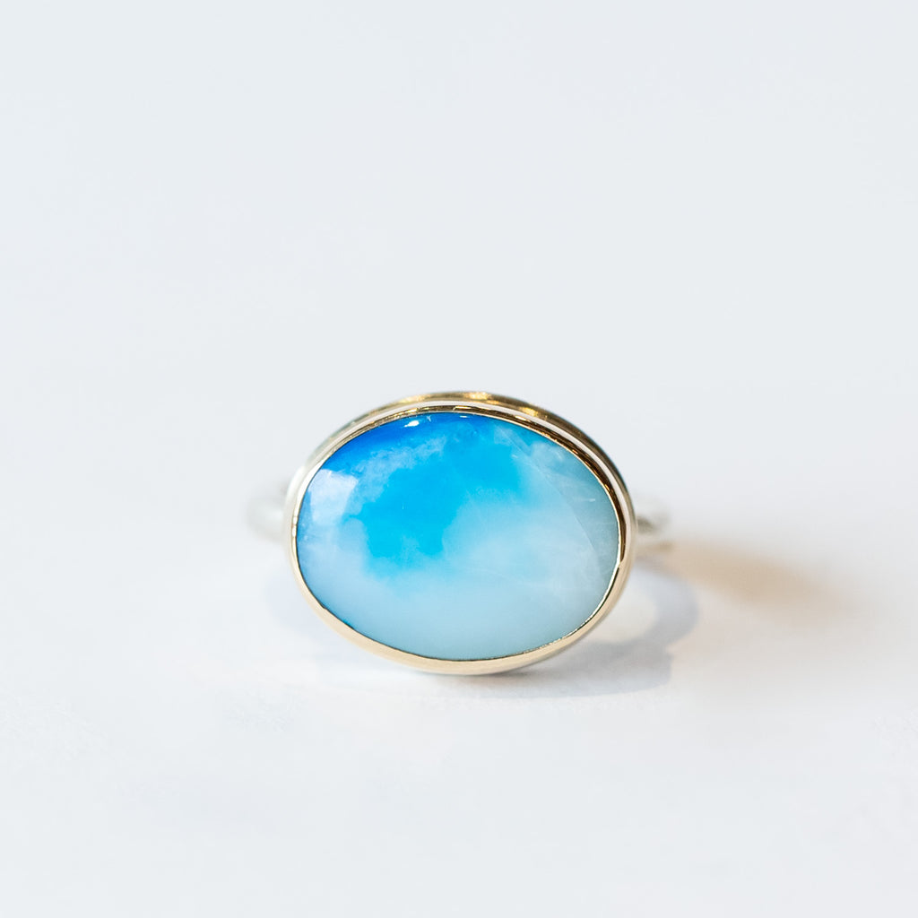 A blue, oval Peruvian opal is bezel set in yellow gold on a silver ring.