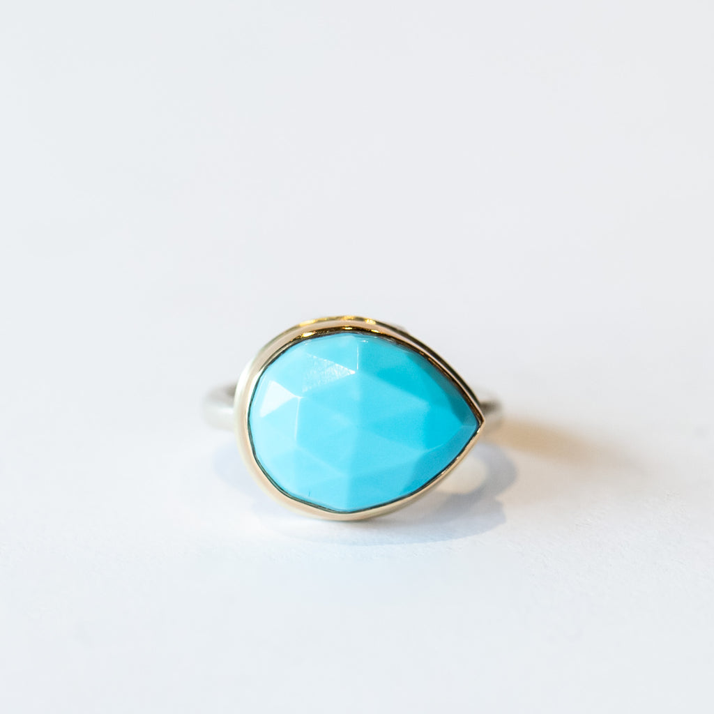 A horizontal-set, rose cut teardrop shaped sleeping beauty turquoise gemstone is bezel set in yellow gold on a silver banded ring.