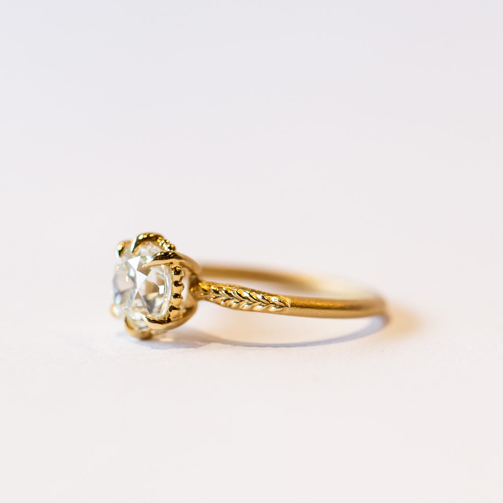 A yellow gold solitaire engagement ring with an old Eurpoean cut diamond and delicate leaf accents on the slender band.