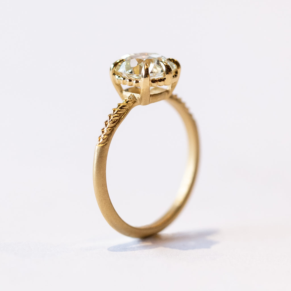A yellow gold solitaire engagement ring with an old Eurpoean cut diamond and delicate leaf accents on the slender band.