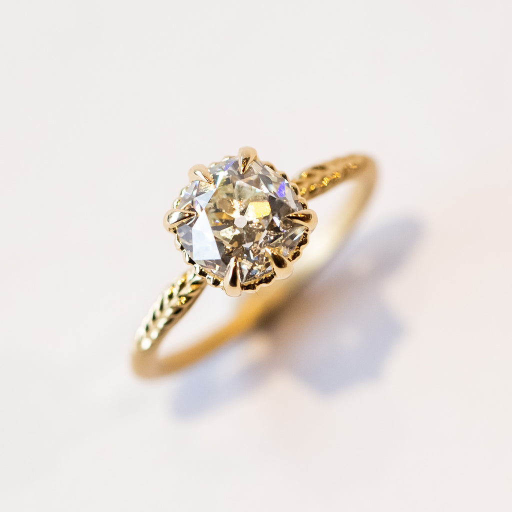 A yellow gold solitaire engagement ring with an old Eurpoean cut diamond and delicate leaf accents on the slender band.