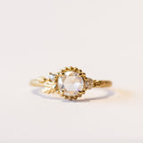 A yellow gold engagement ring with a round, rose cut center diamond accented by asymmetrical foliate elements and two small side diamonds.