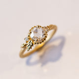 A yellow gold engagement ring with a round, rose cut center diamond accented by asymmetrical foliate elements and two small side diamonds.