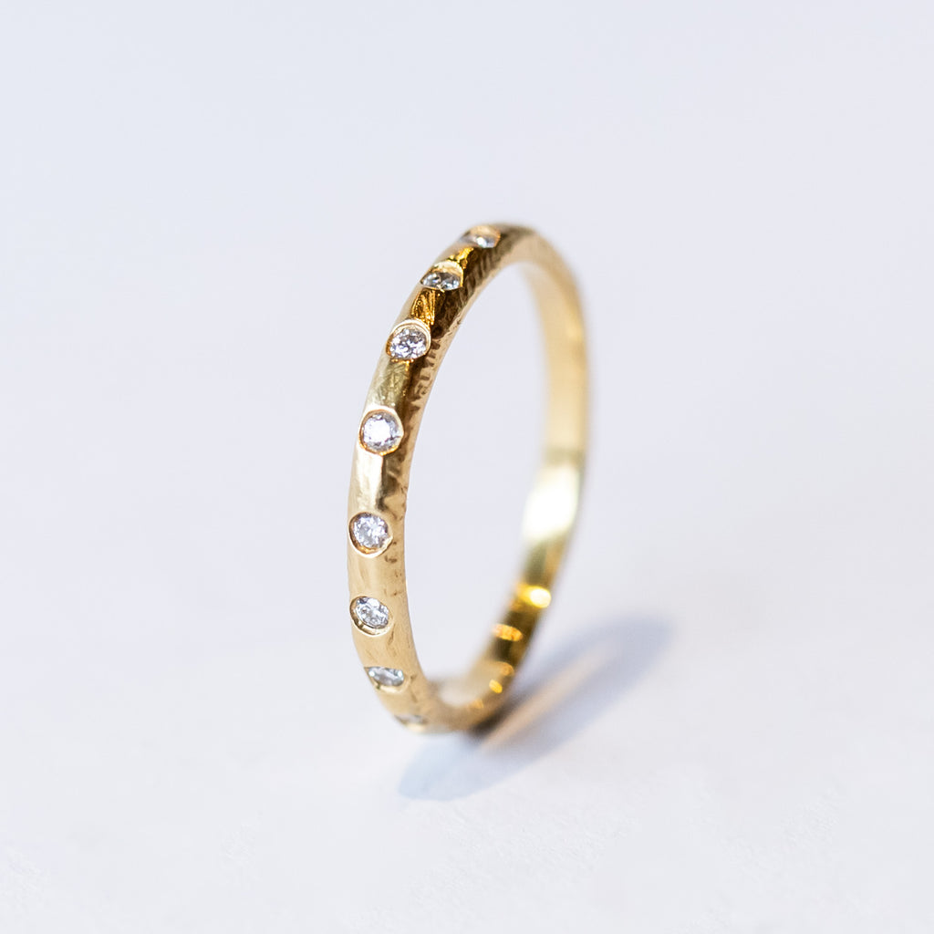 A textured yellow gold wedding band with flush set diamonds all the way around.