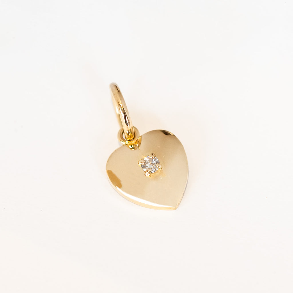 A yellow gold heart charm with a single round diamond set in the center.