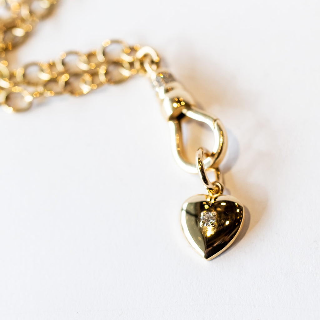 A yellow gold heart charm with a single round diamond set in the center.