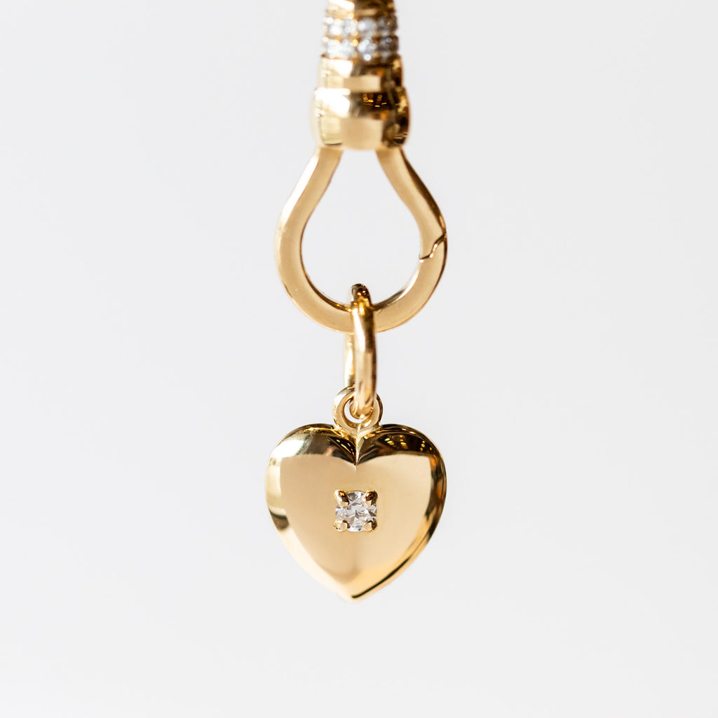 A yellow gold heart charm with a single round diamond set in the center.
