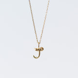 A tiny snake forms a letter "J" pendant in yellow gold on a cable chain necklace.