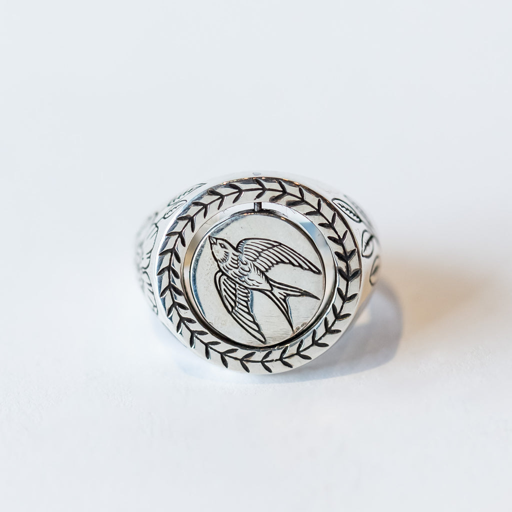 A chunky silver signet ring with engraved design of a bird on a spinning center plate which has a rabbit on the other side, surrounded by floral motifs.