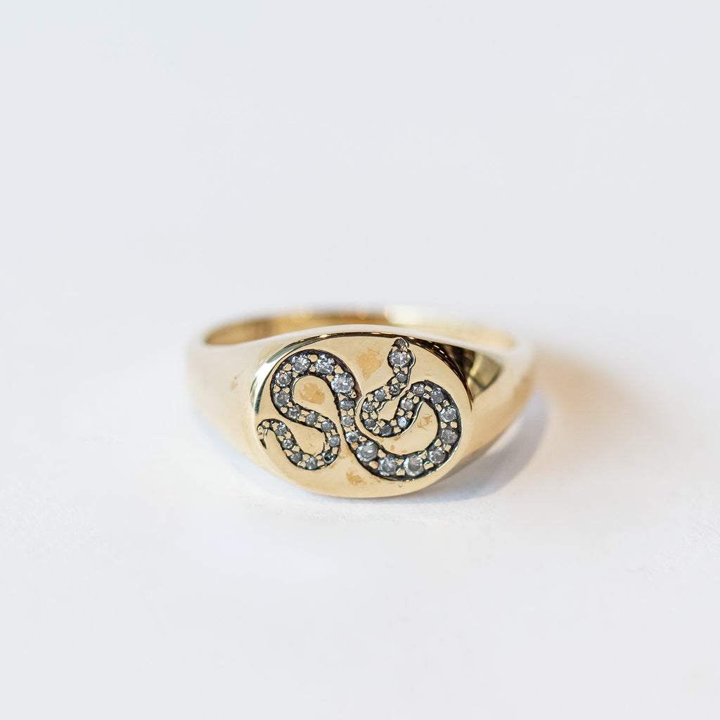 A gold signet ring with an engraved snake set with salt and pepper diamonds.
