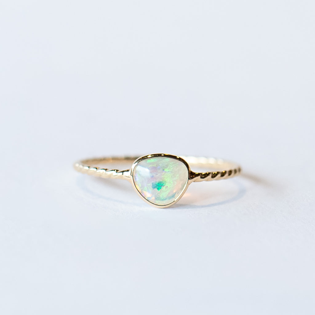 An asymmetrical opal is bezel set into a twist-design thin gold ring.
