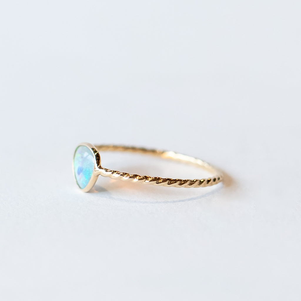 An asymmetrical opal is bezel set into a twist-design thin gold ring.