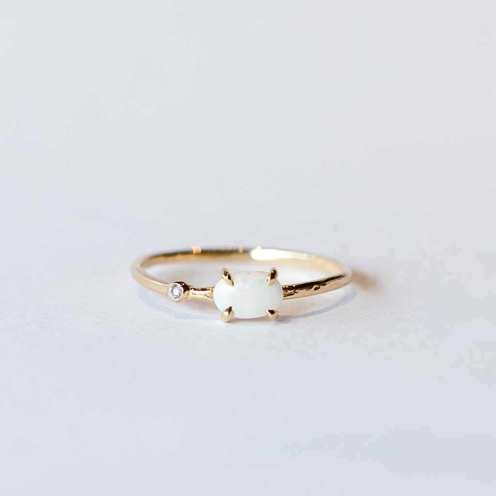 A thin yellow gold stacking ring with a small prong set white opal and a petite bezel set diamond to one side.
