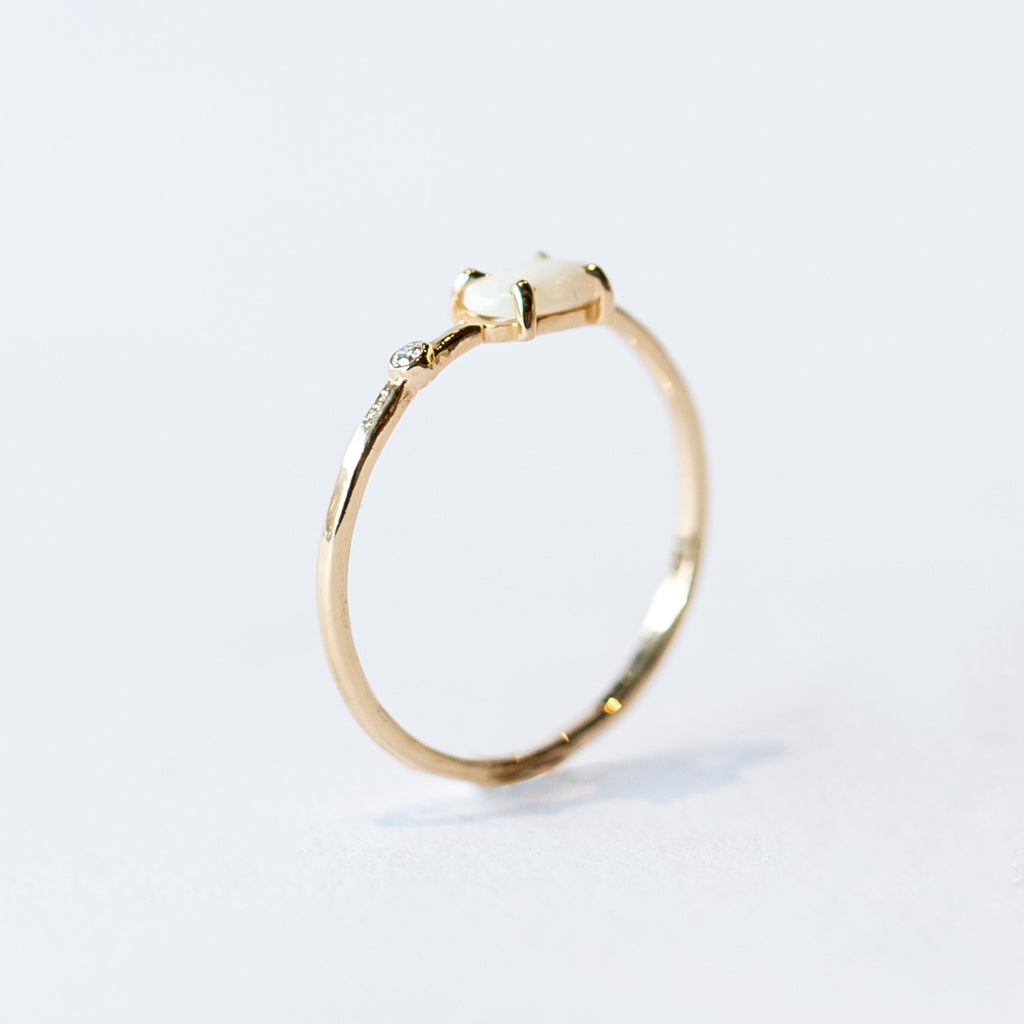 A thin yellow gold stacking ring with a small prong set white opal and a petite bezel set diamond to one side.