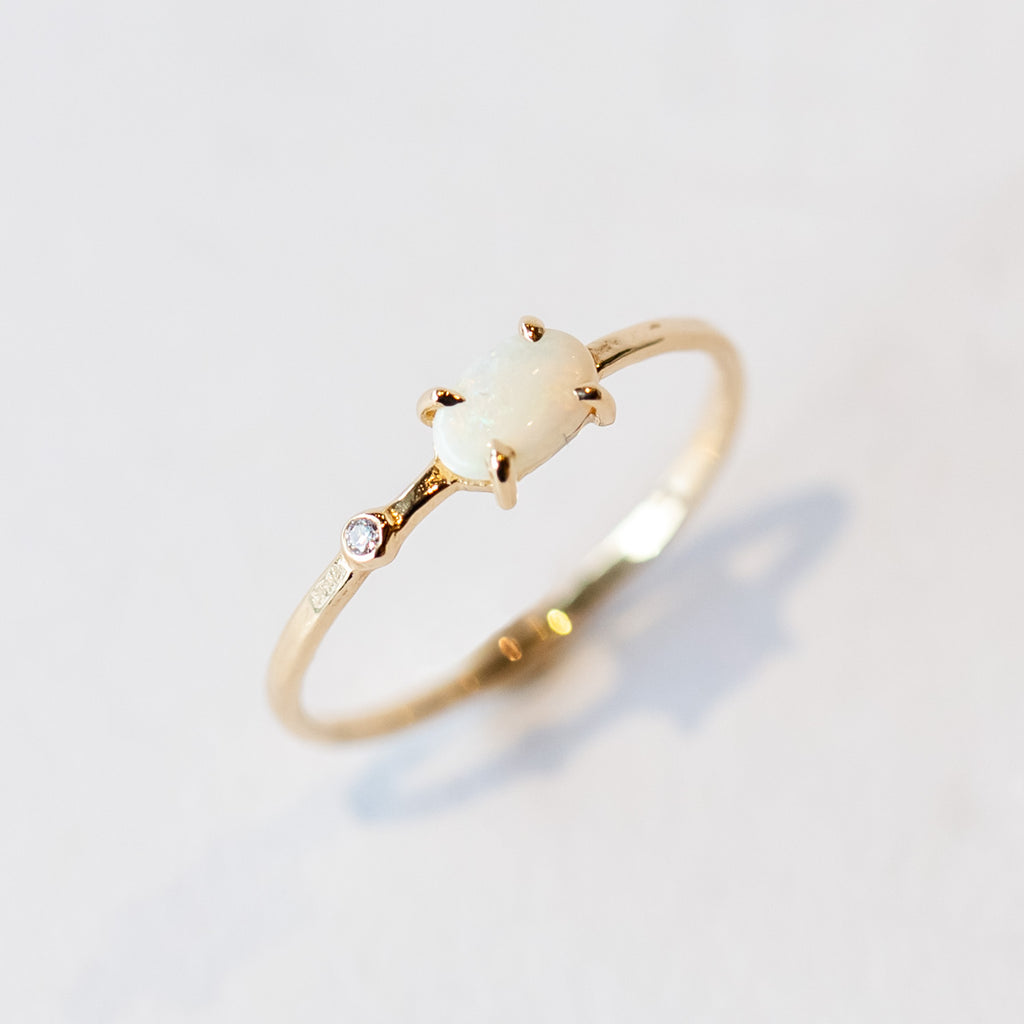 A thin yellow gold stacking ring with a small prong set white opal and a petite bezel set diamond to one side.