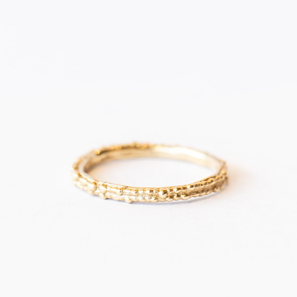 A thin, decorative gold band displaying two rows of organic beaded details.