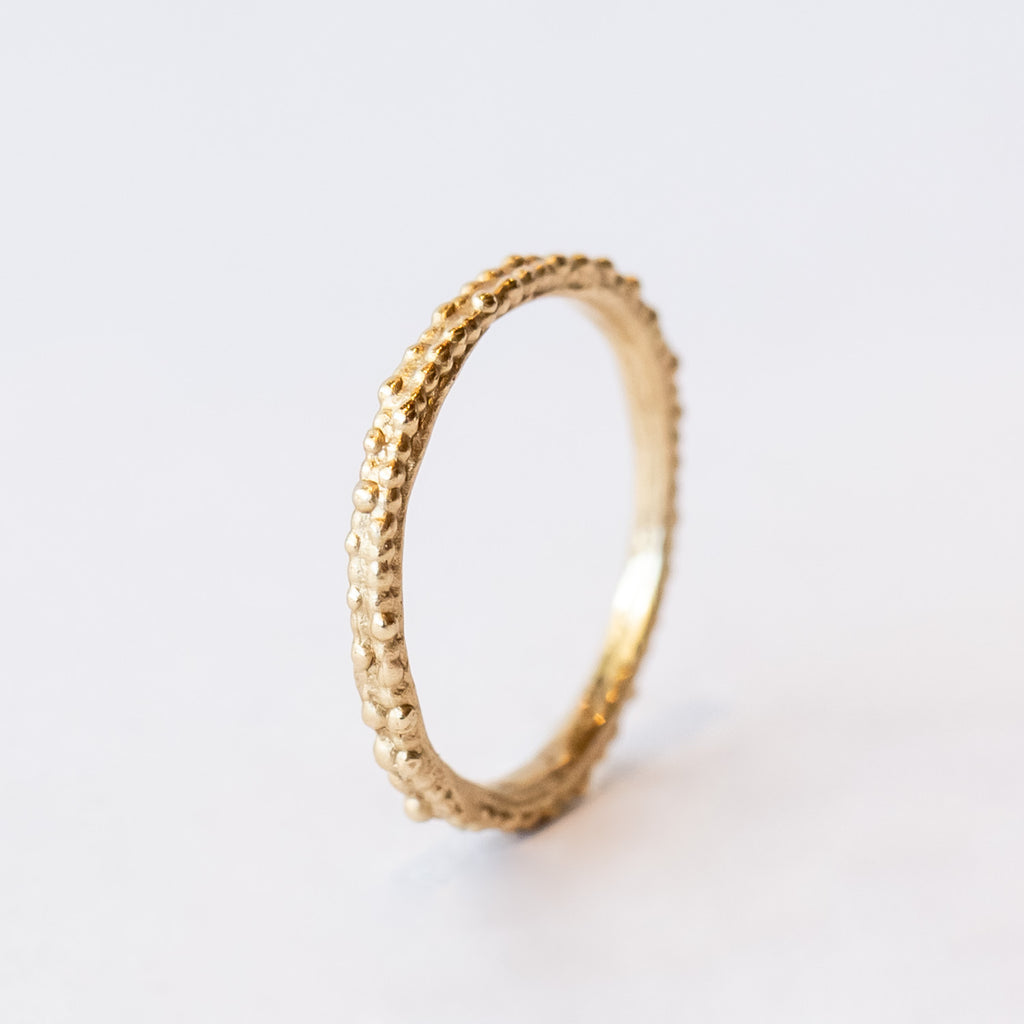 A thin, decorative gold band displaying two rows of organic beaded details.