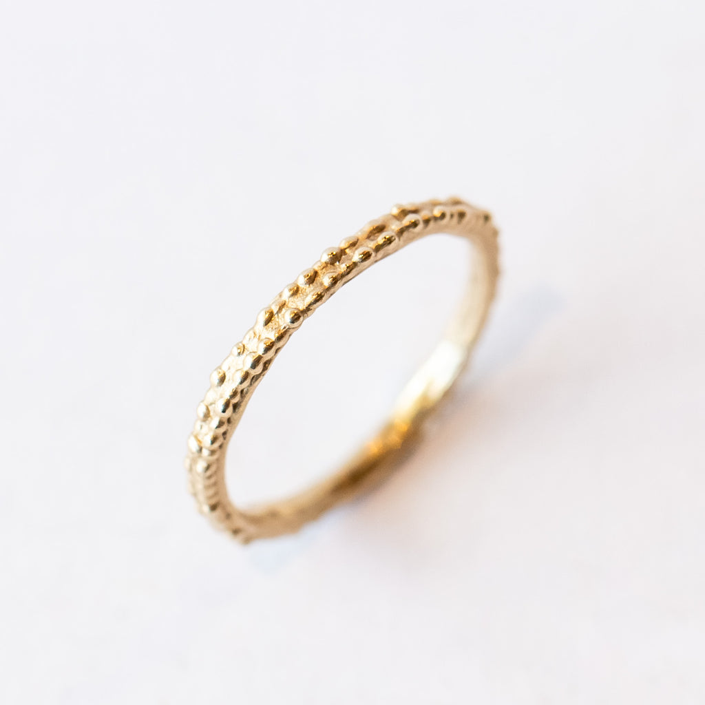 A thin, decorative gold band displaying two rows of organic beaded details.