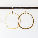 A large, open gold circle hoop hangs from a tiny diamond dot on an ear hook.