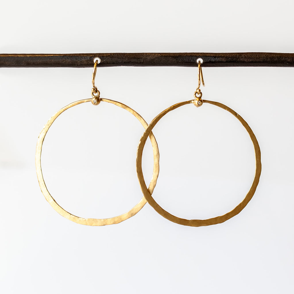 A large, open gold circle hoop hangs from a tiny diamond dot on an ear hook.