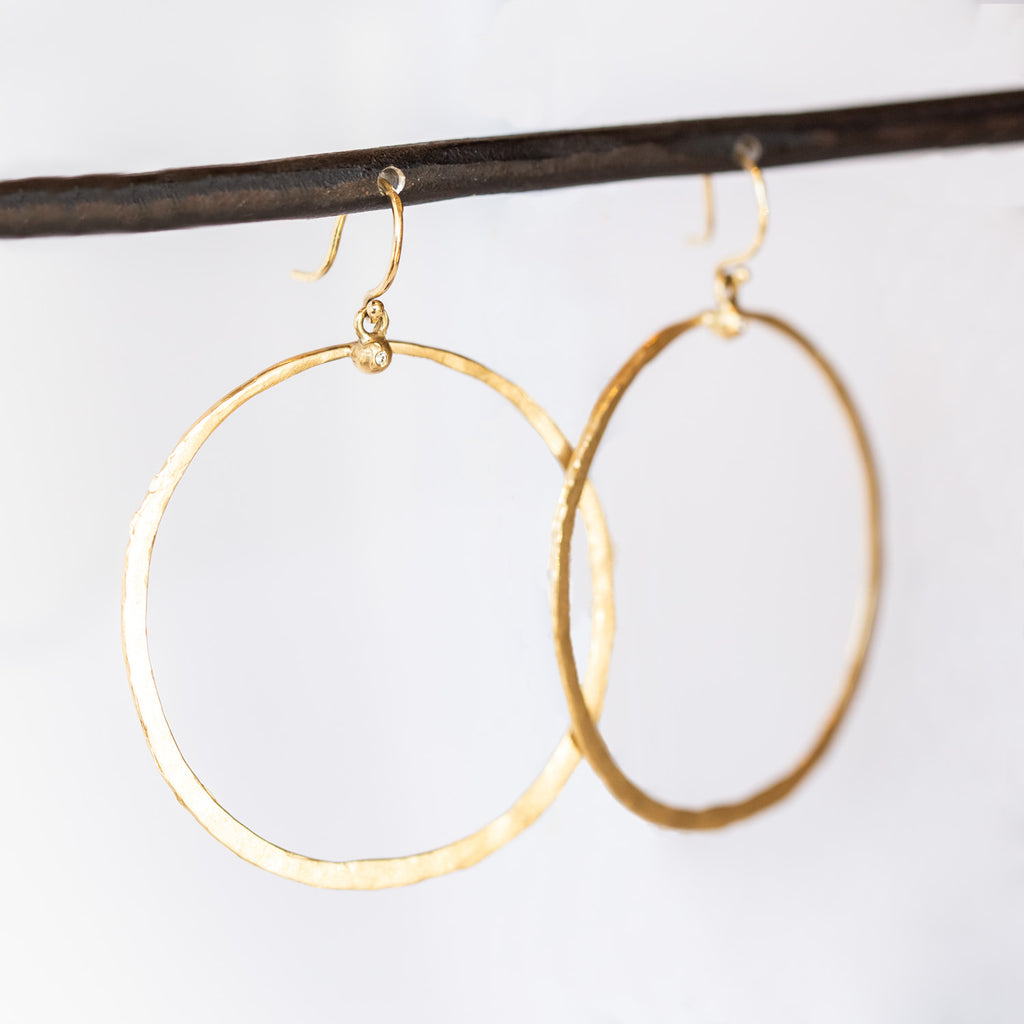 A large, open gold circle hoop hangs from a tiny diamond dot on an ear hook.