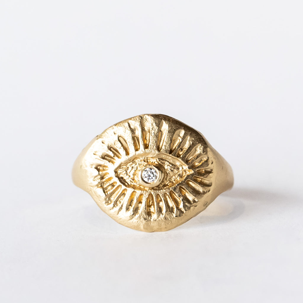 Yellow gold signet ring with hand carved eye design with a small diamond in the middle.