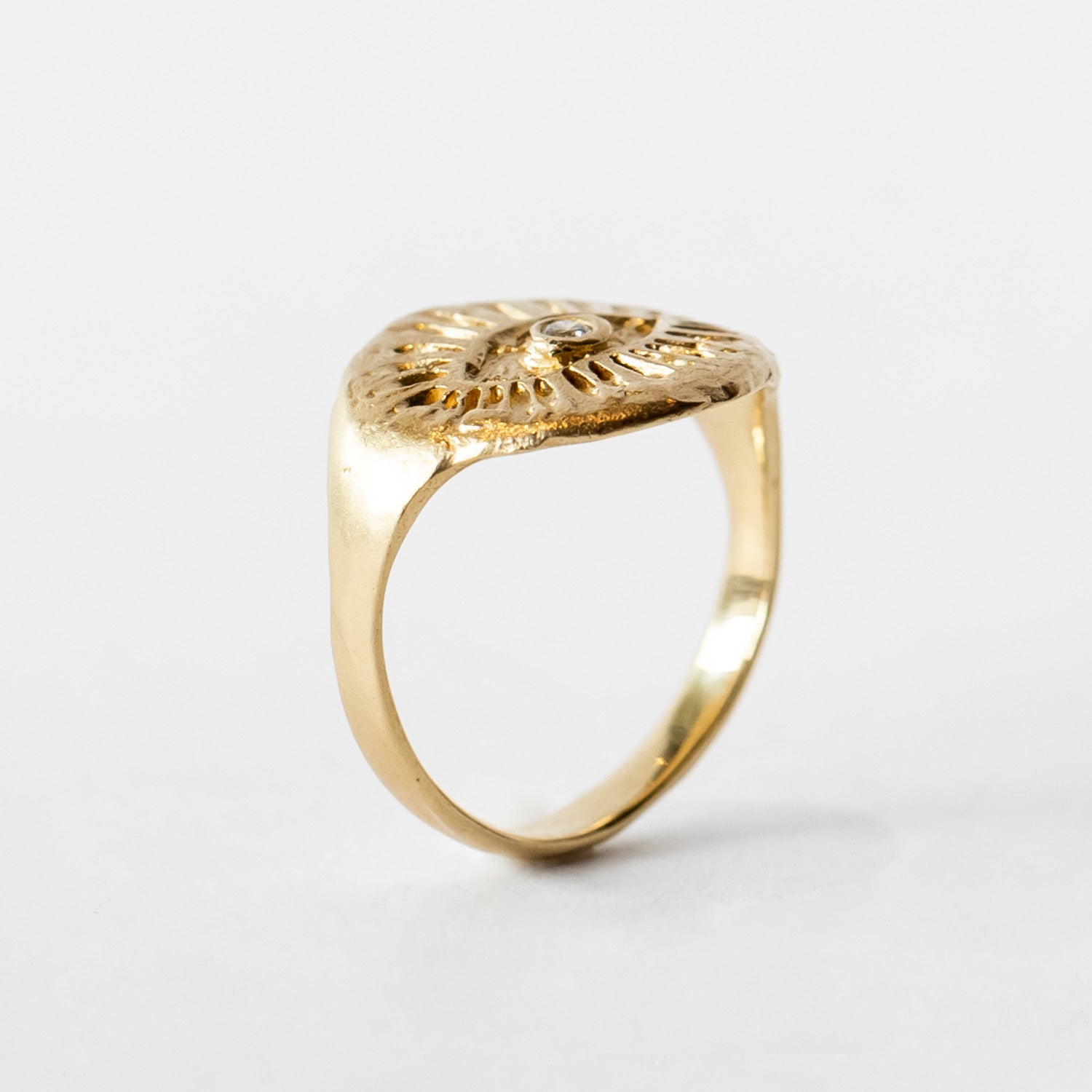 Yellow gold signet ring with hand carved eye design with a small diamond in the middle.