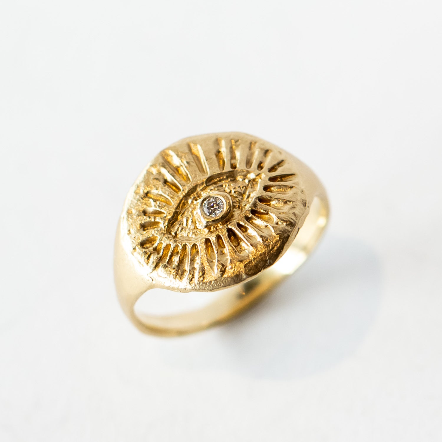 Yellow gold signet ring with hand carved eye design with a small diamond in the middle.