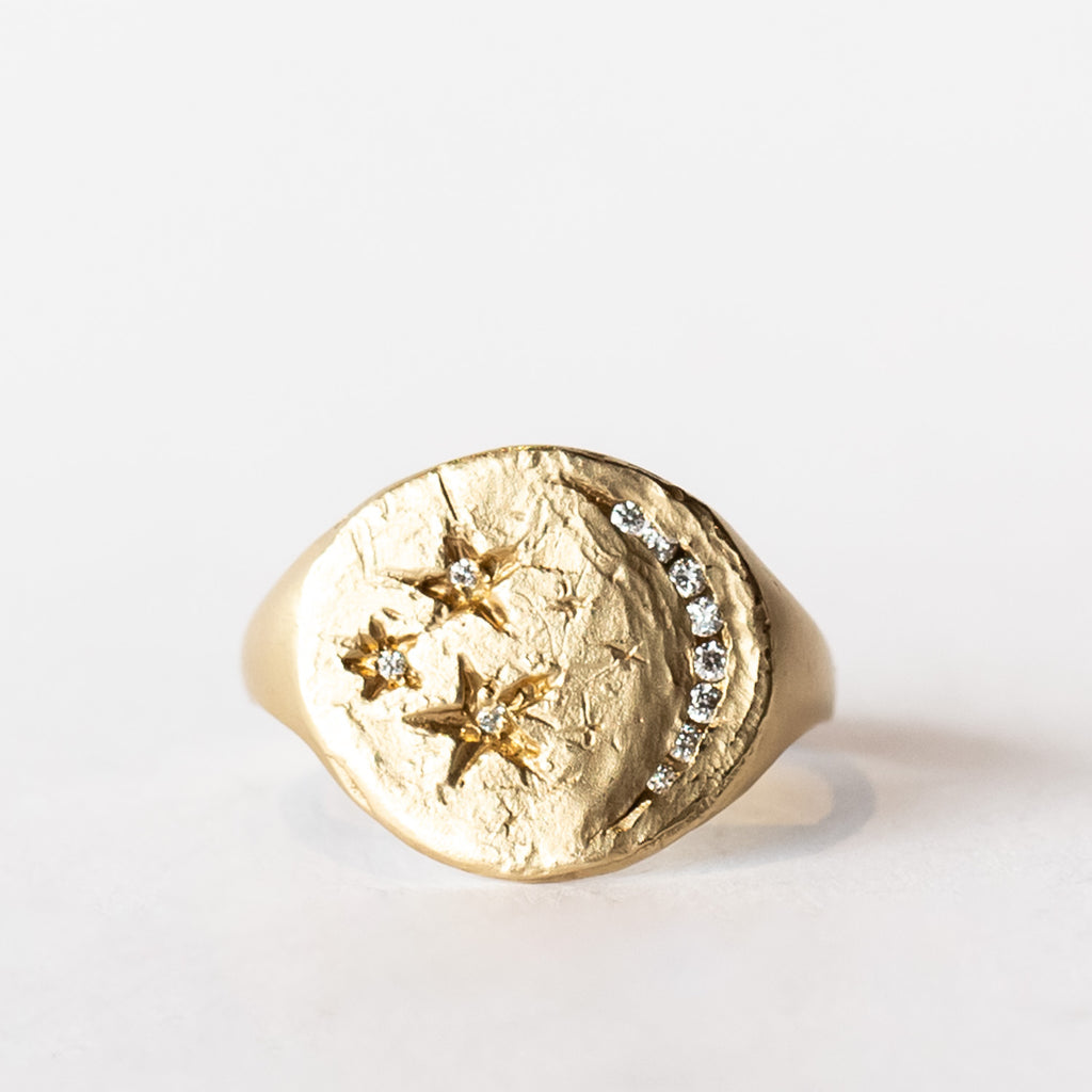 A hand carved yellow gold signet ring with a crescent moon and stars design with diamonds.