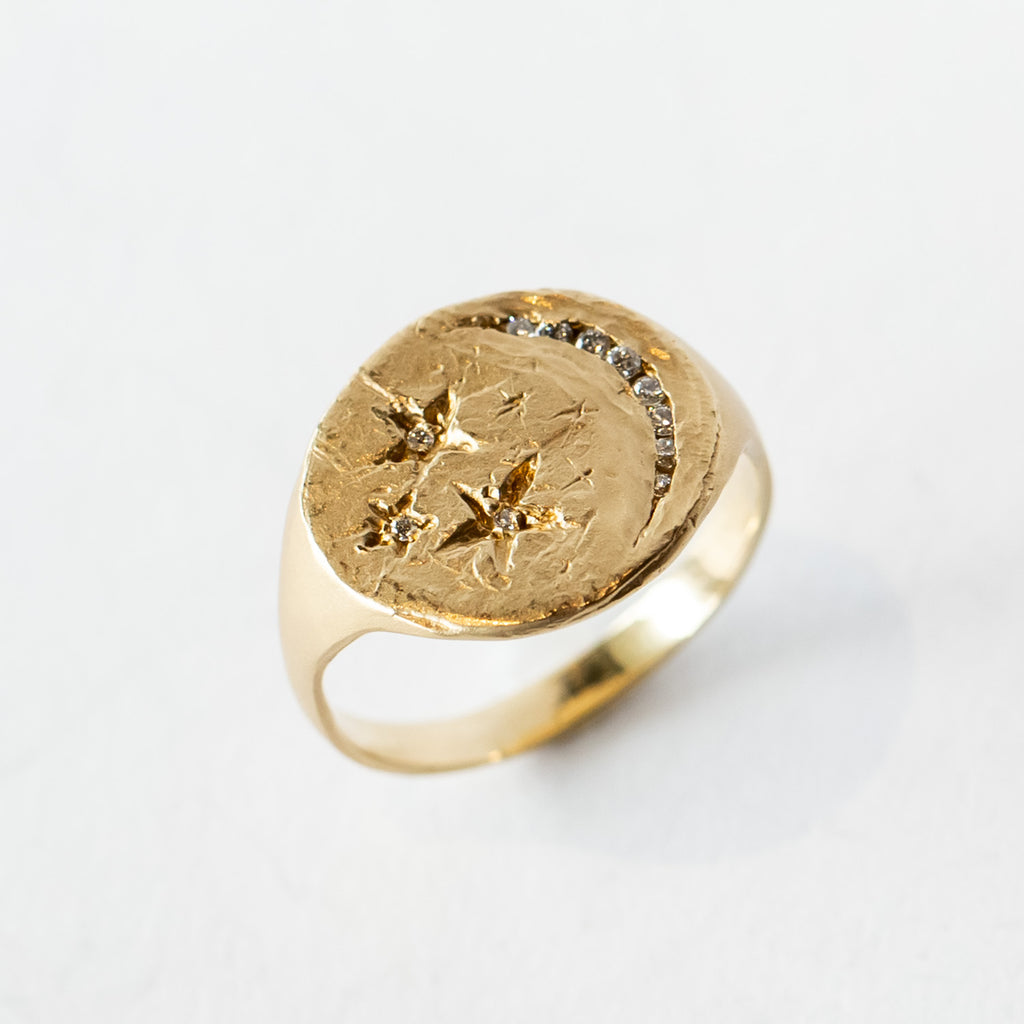 A hand carved yellow gold signet ring with a crescent moon and stars design with diamonds.