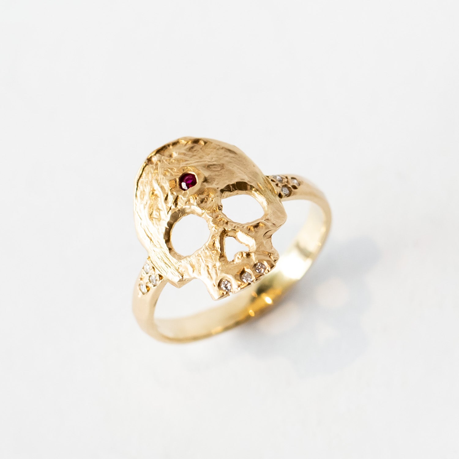 A hand carved gold ring with a skull shaped top, set with diamond teeth and a ruby on the forehead.