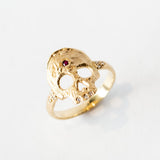 A hand carved gold ring with a skull shaped top, set with diamond teeth and a ruby on the forehead.