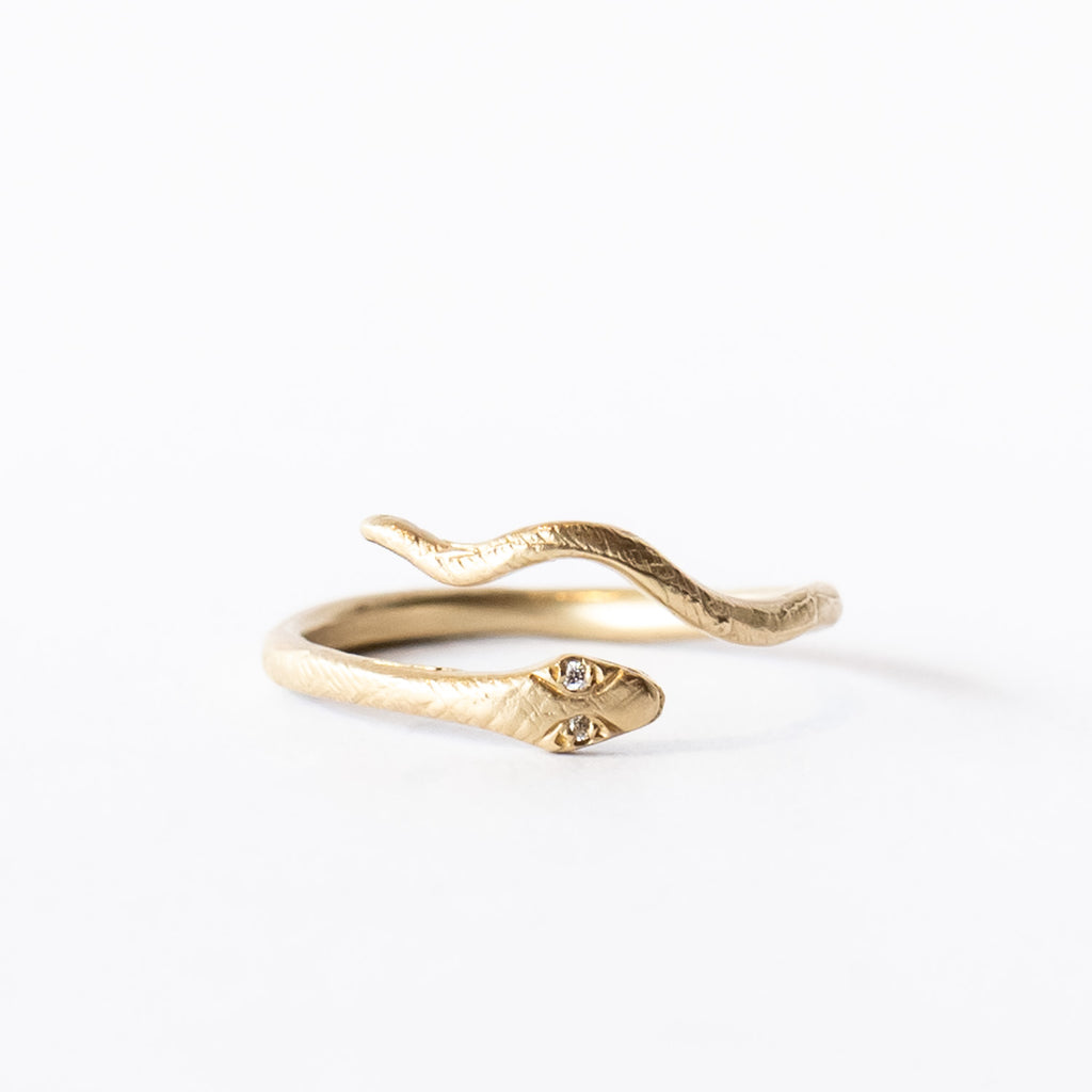 A slender yellow gold snake ring with diamond eyes that wraps around the finger.