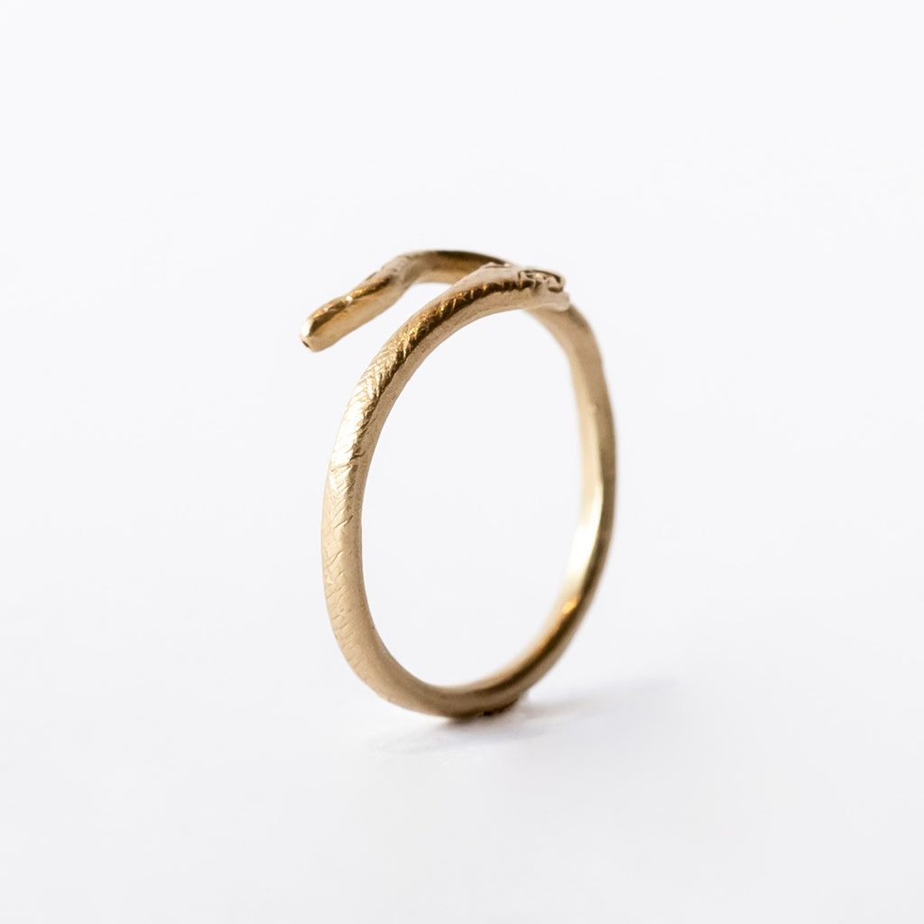 A slender yellow gold snake ring with diamond eyes that wraps around the finger.