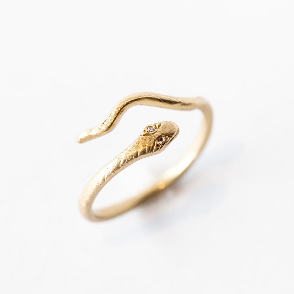 A slender yellow gold snake ring with diamond eyes that wraps around the finger.
