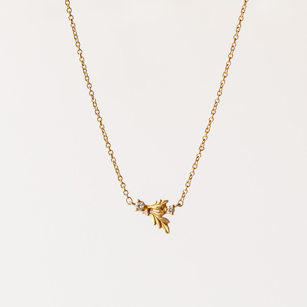 A delicate gold chain necklace featuring a leaf-like station set with three tiny diamonds.