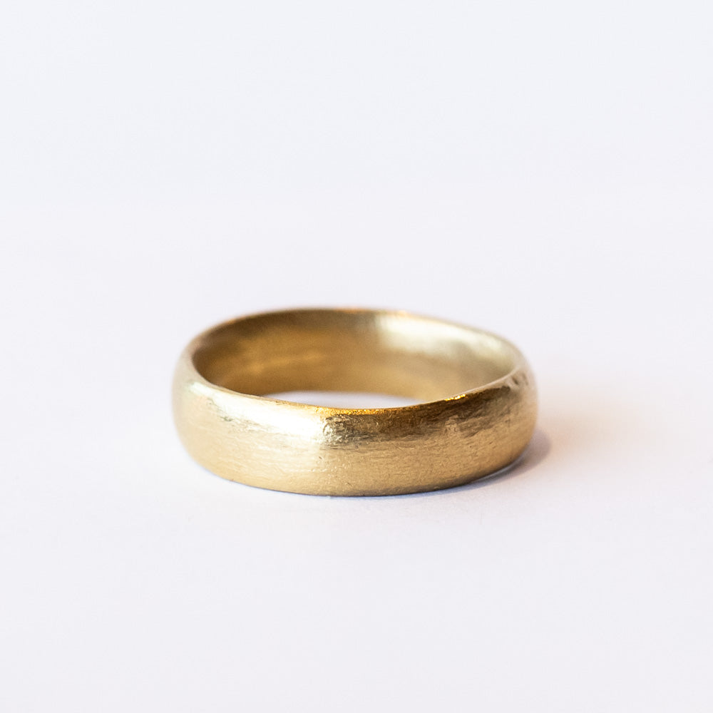 A wide, softly textured yellow gold wedding band.