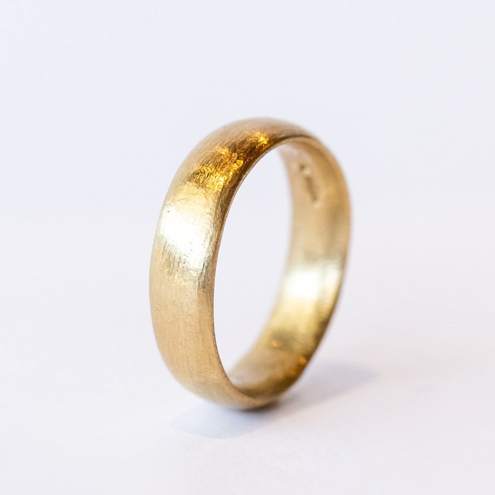 A wide, softly textured yellow gold wedding band.