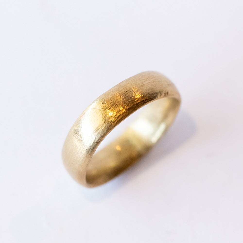 A wide, softly textured yellow gold wedding band.
