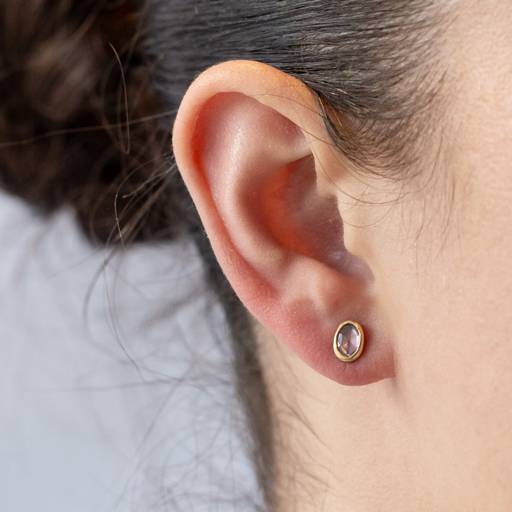 A pair of asymmetrical pink sapphire stud earrings set in yellow gold bezels. On model.