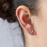 A pair of asymmetrical pink sapphire stud earrings set in yellow gold bezels. On model.