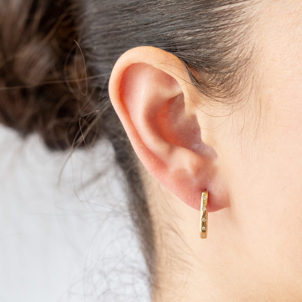 Textured yellow gold hoop earrings set with small diamonds down the front. On model.