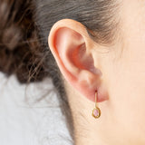 Dainty yellow gold drop earrings featuring oval pink sapphires in textured bezels. On model.